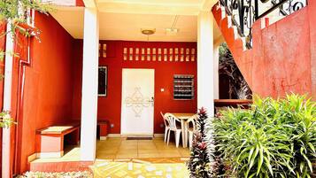 A red building with a white door, a tiled patio, and a staircase.