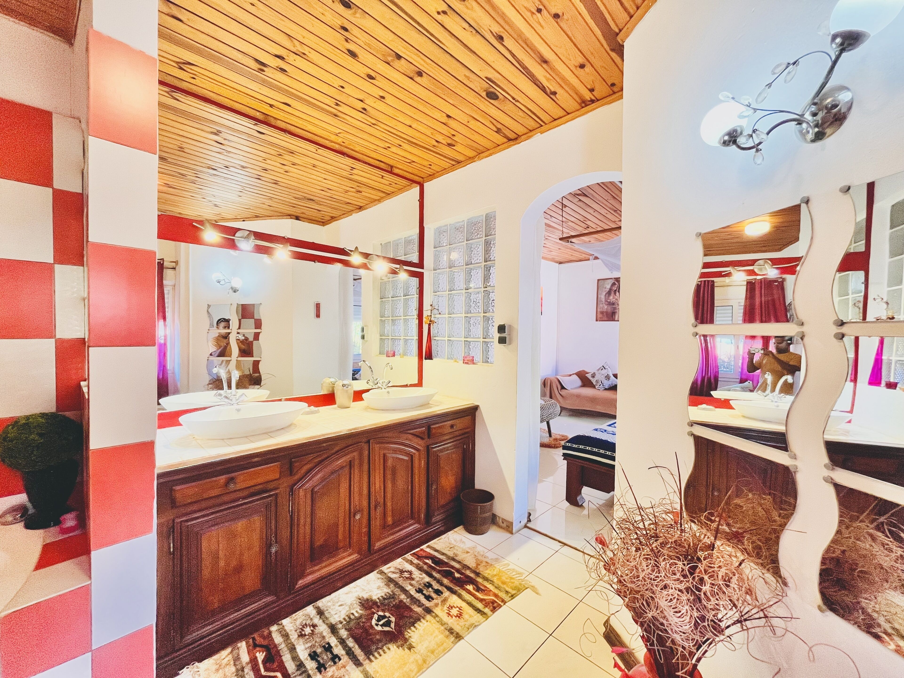 Une salle de bain avec un plafond en bois, un grand miroir et un mur à carreaux rouges et blancs.