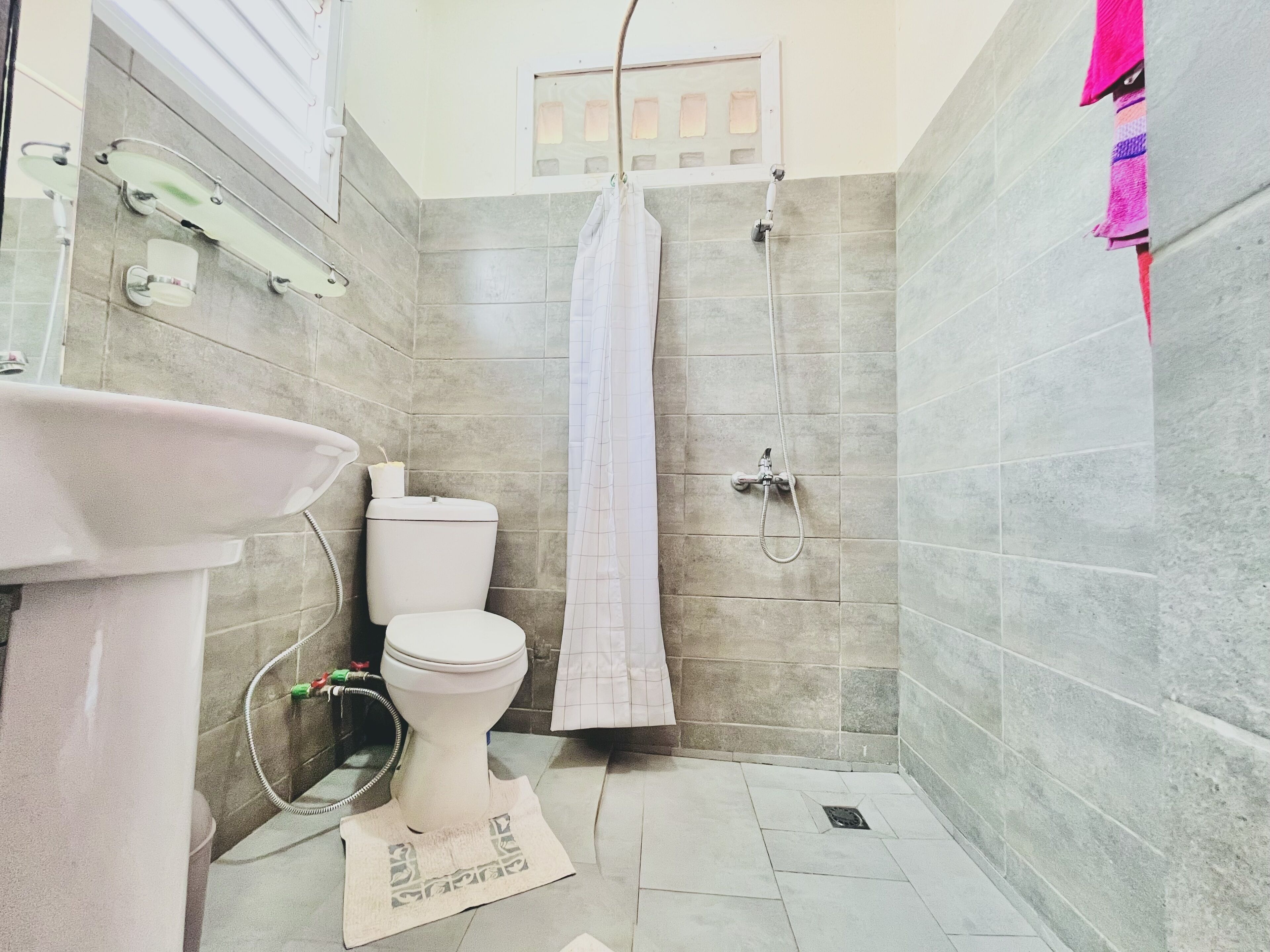 A small, tiled bathroom with a toilet, sink, and shower.