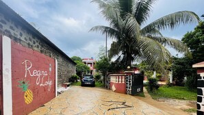 A paved driveway leading to a gated entrance with a stone wall and a sign reading "Regina Lodge". - Régina Lodge (Antsiranana)