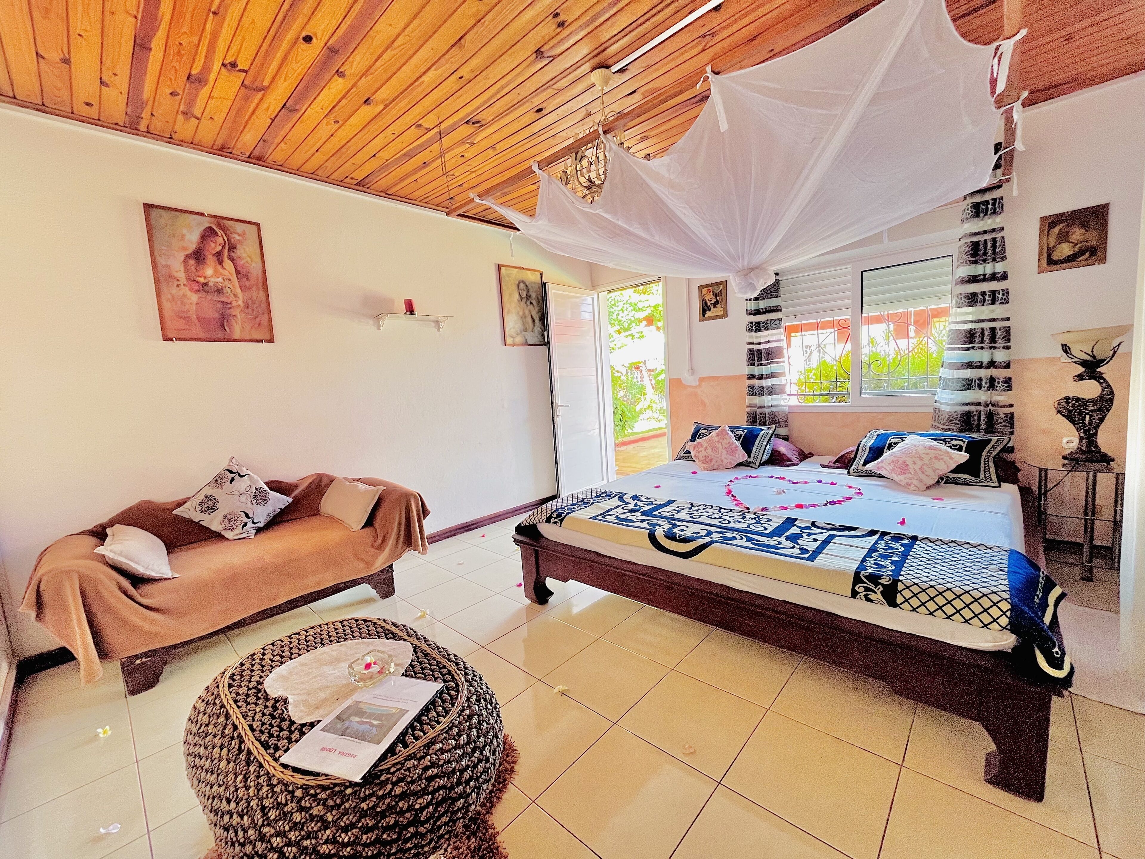 A bedroom with a bed, a sofa, and a wicker ottoman.