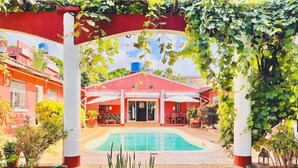 A pool area with a red building, covered patio, and surrounding greenery. - Régina Lodge (Antsiranana)