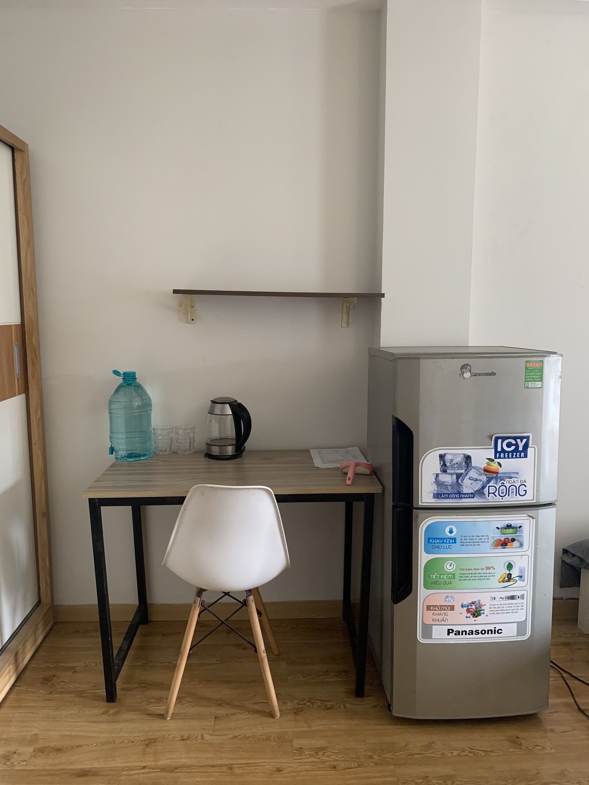 A small kitchenette with a fridge, a table, a chair, and a water bottle.