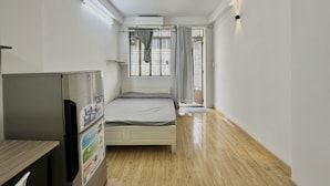 A compact room with a bed, a refrigerator, and a window with curtains. - Homestay 26 Nguyen Van Lac (Ho Chi Minh City)