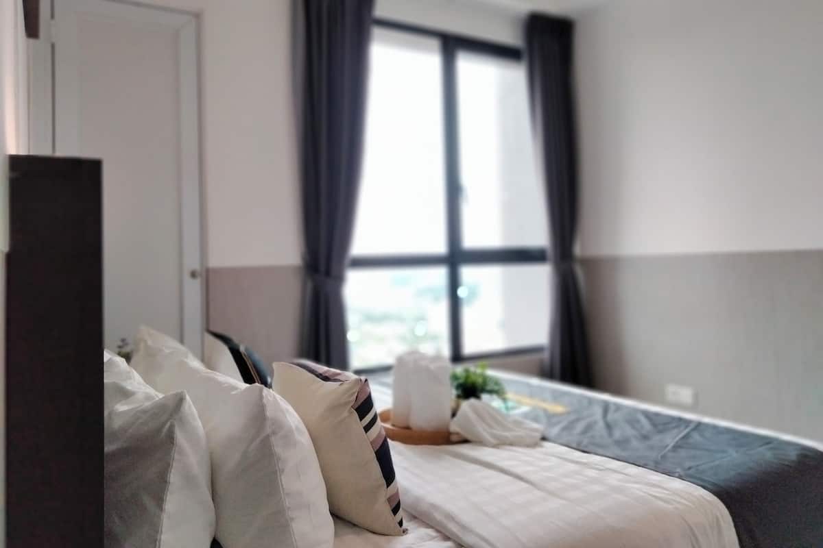 A hotel room with a bed, pillows, a window with curtains, and a door.