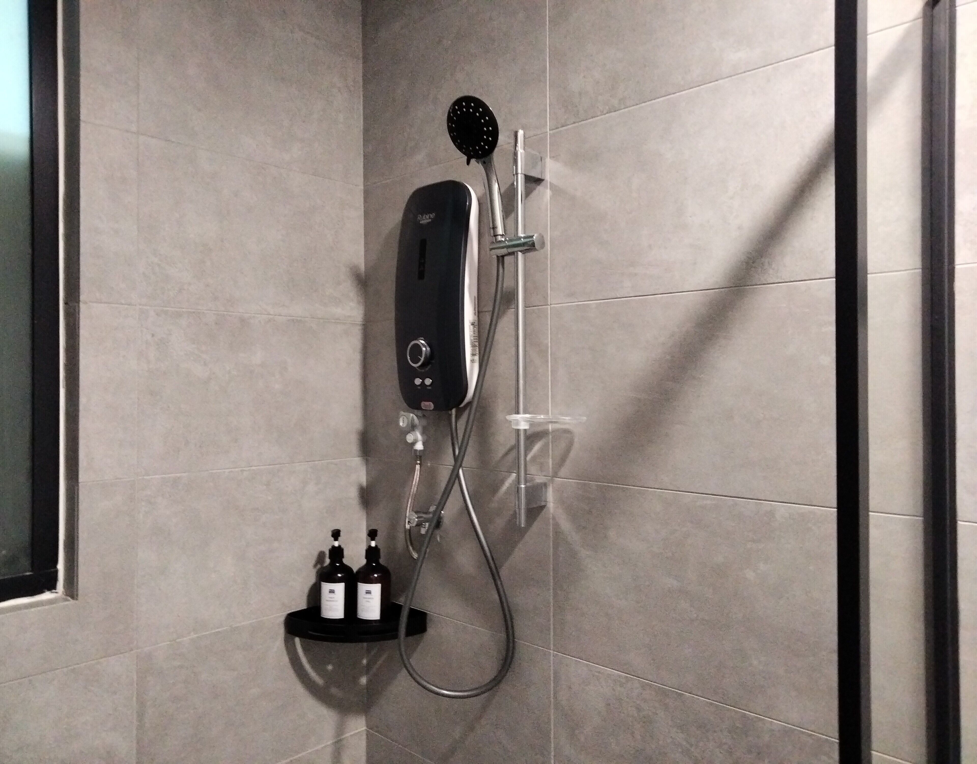A modern shower with a handheld showerhead, a wall-mounted control panel, and a soap dispenser.