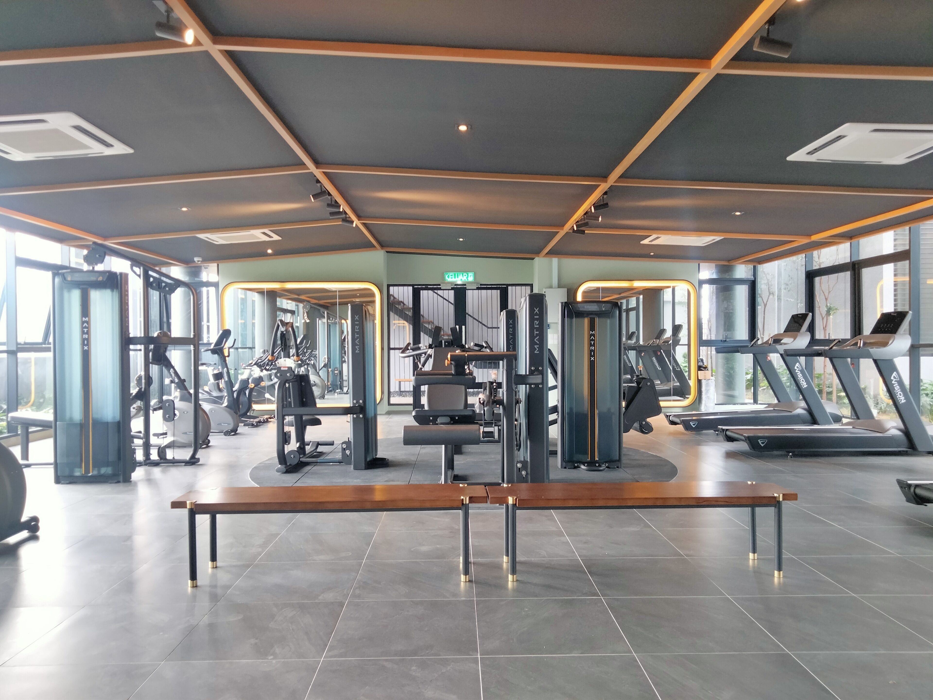 Une salle de sport équipée de divers appareils d’exercice, d’un banc et de grandes fenêtres laissant entrer la lumière naturelle.