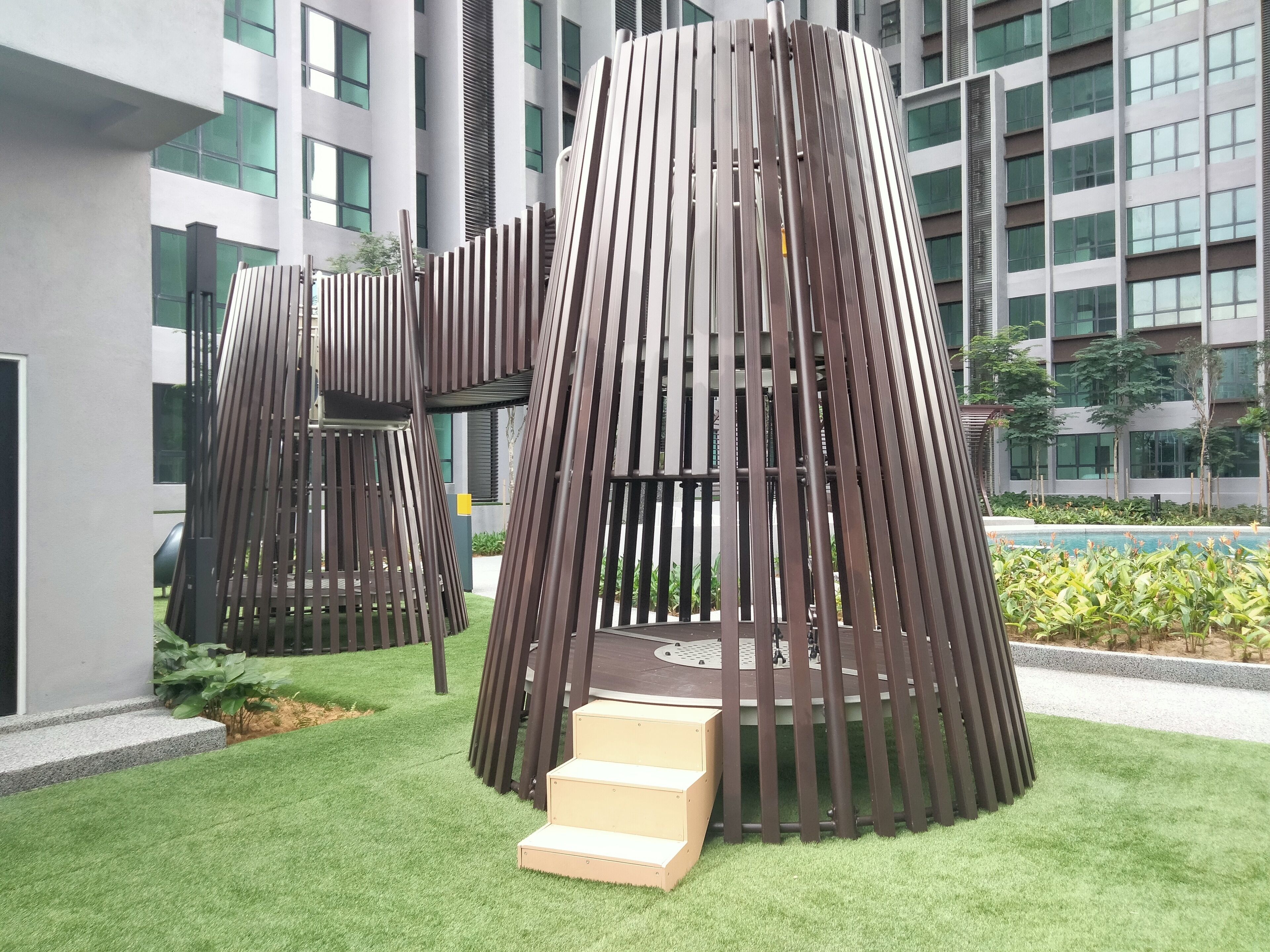 A modern outdoor structure with vertical slats, surrounded by artificial grass and a pool.