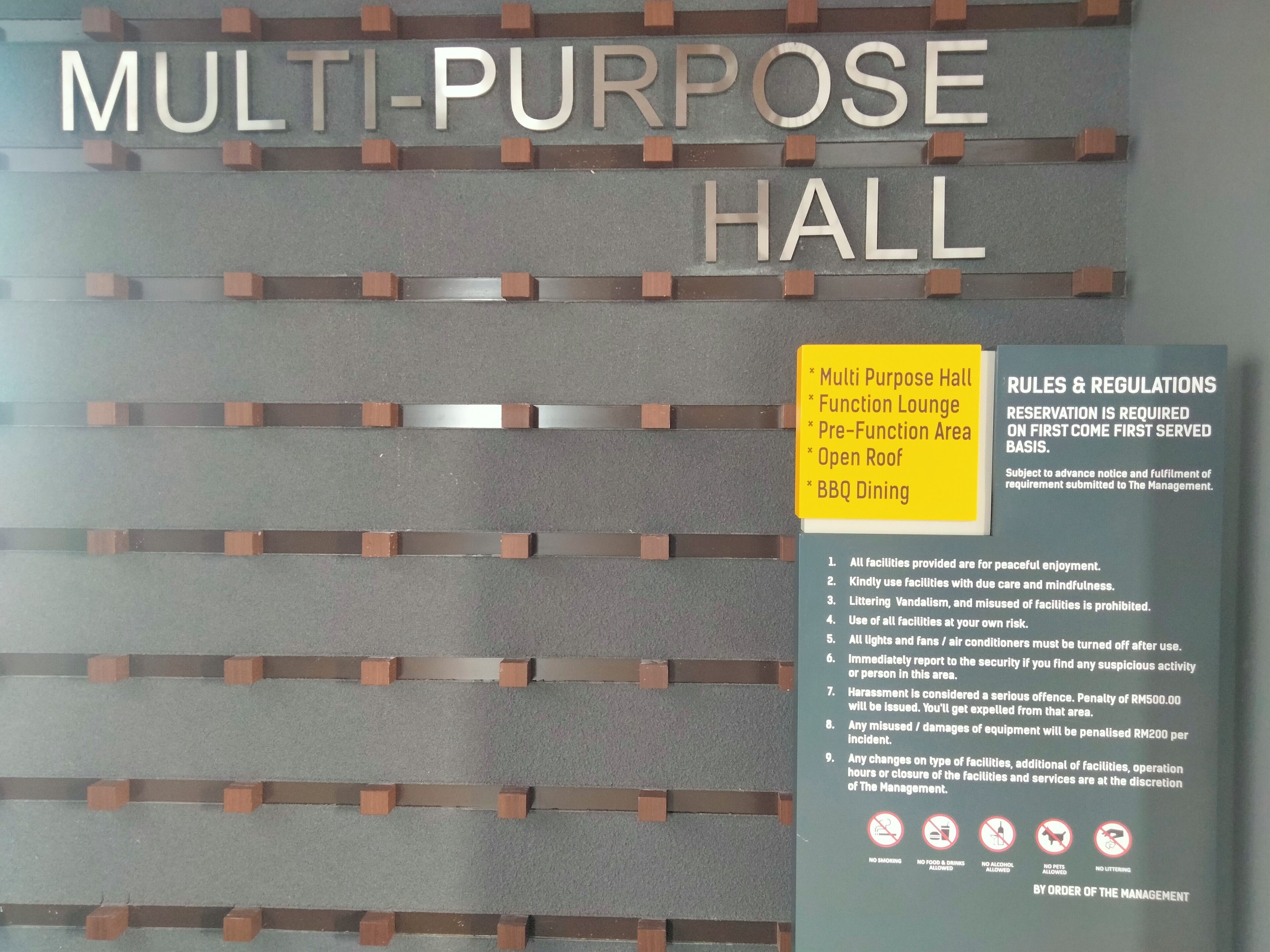 Une salle polyvalente dont une pancarte indique les équipements disponibles, notamment un salon pour les événements, un espace barbecue et un toit ouvrant.
