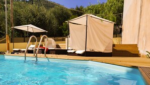 Ein Schwimmbecken mit Holzterrasse, Liegestühlen und einer überdachten Sitzgelegenheit.