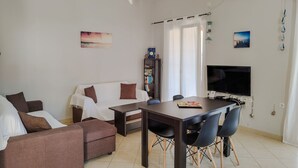 Ein Wohnzimmer mit einer Couch, einem Esstisch mit Stühlen, einem Fernseher und einem Bücherregal.