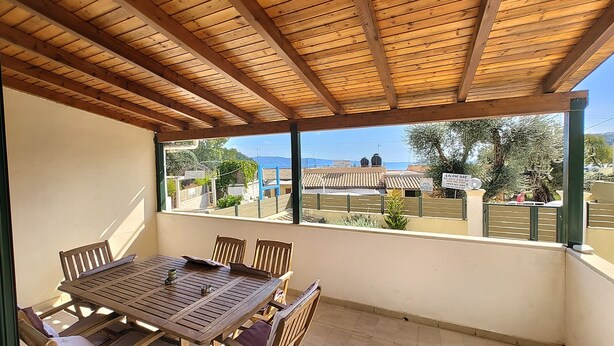 Eine überdachte Terrasse mit Holztisch und -stühlen, Blick auf eine Stadt und einem klaren Himmel.
