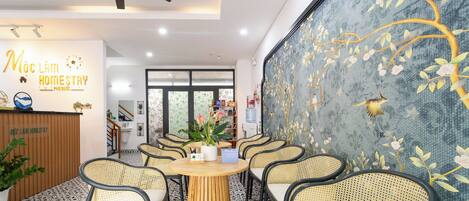 A cozy indoor seating area with wicker chairs and a central wooden table, surrounded by a patterned floor and a decorative wall mural.