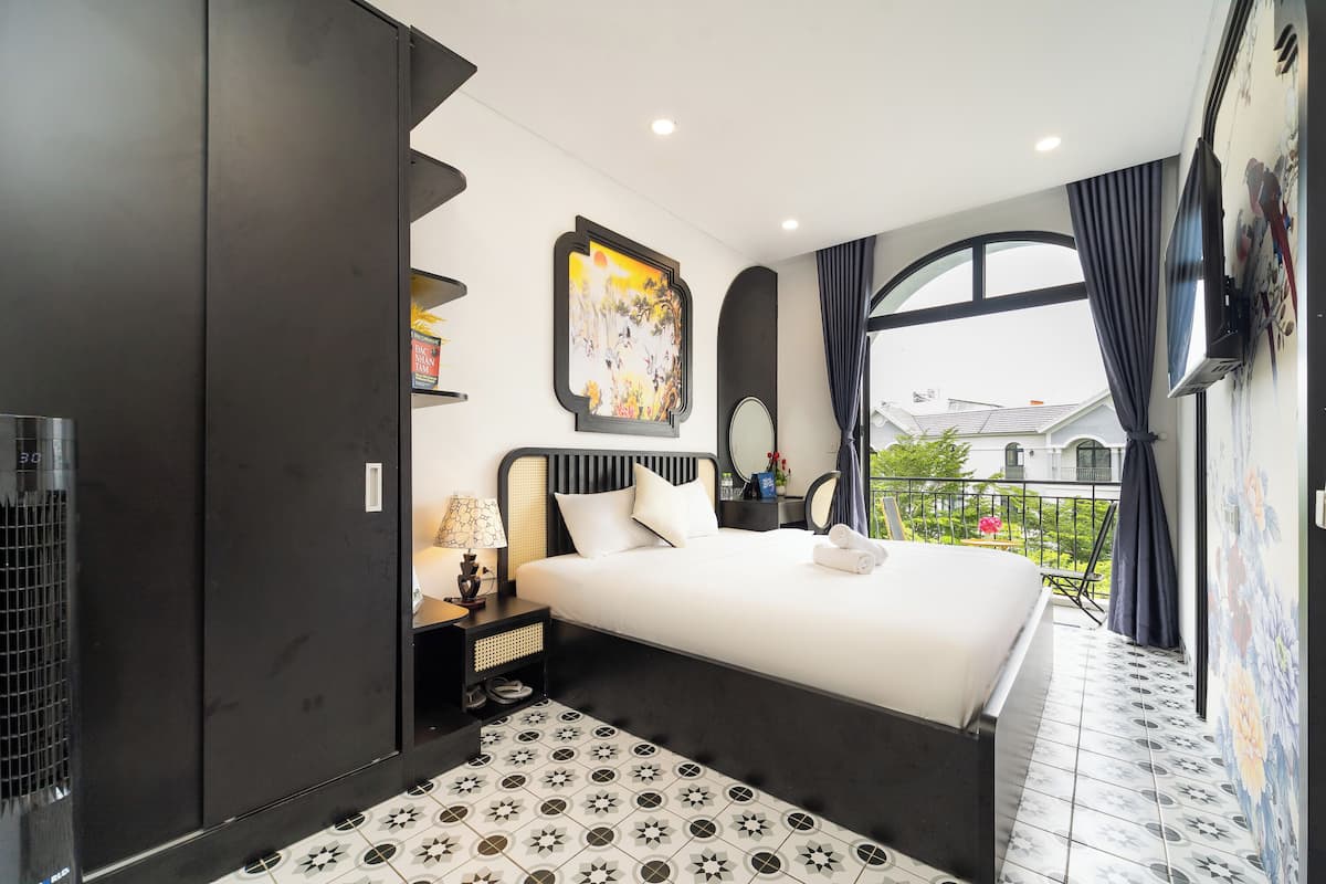 A modern hotel room with a large bed, a flat-screen TV, a balcony with a view, and a decorative painting.