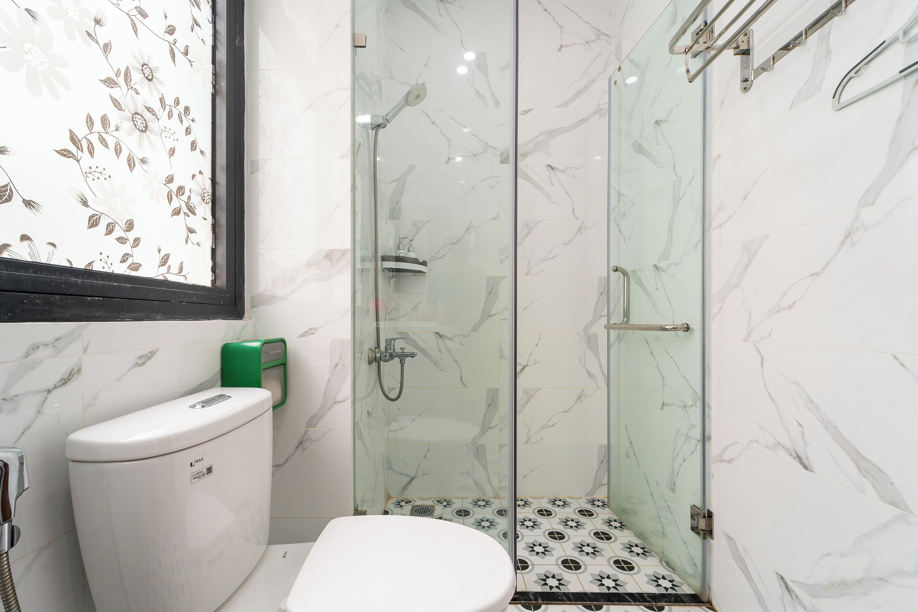 Un baño con inodoro, ducha con cerramiento de vidrio y suelo de baldosas de mármol.