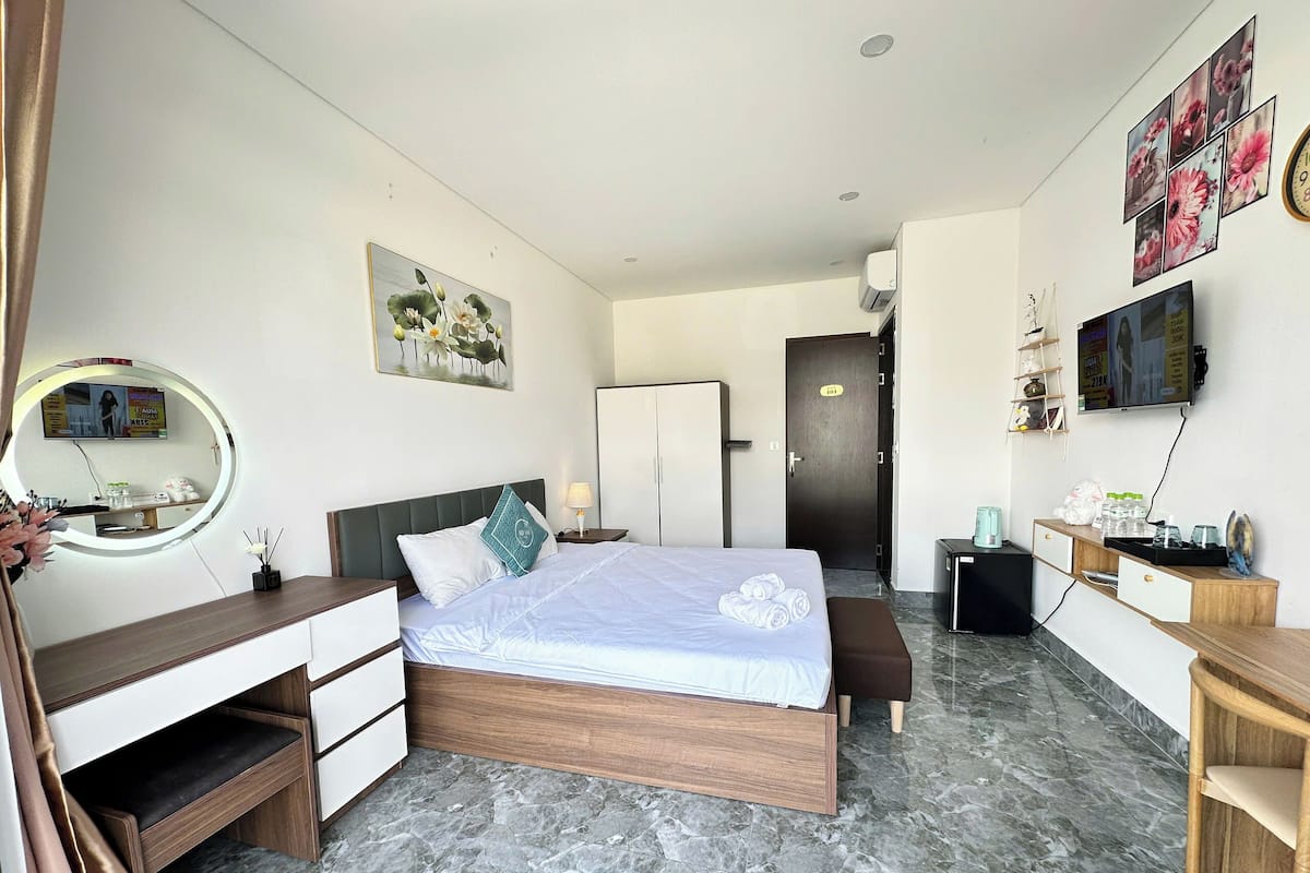 A modern hotel room with a bed, bedside table, mirror, and a TV on the wall.