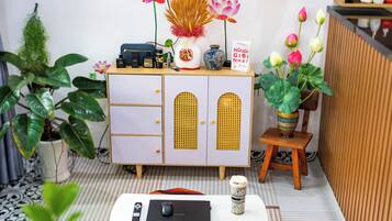 Una habitación ordenada con una mesa blanca, un mueble con cajones, un taburete pequeño y plantas en macetas.