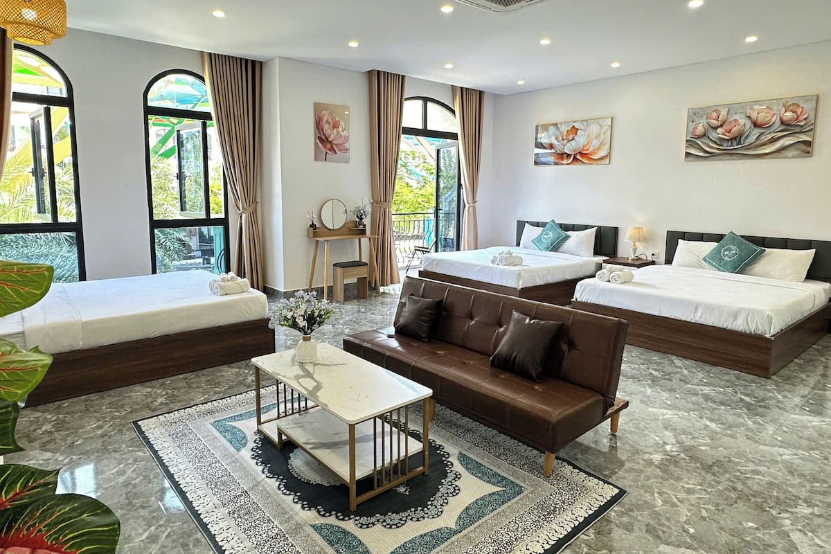 A hotel room with a sofa, two single beds, a small table, and a large window.