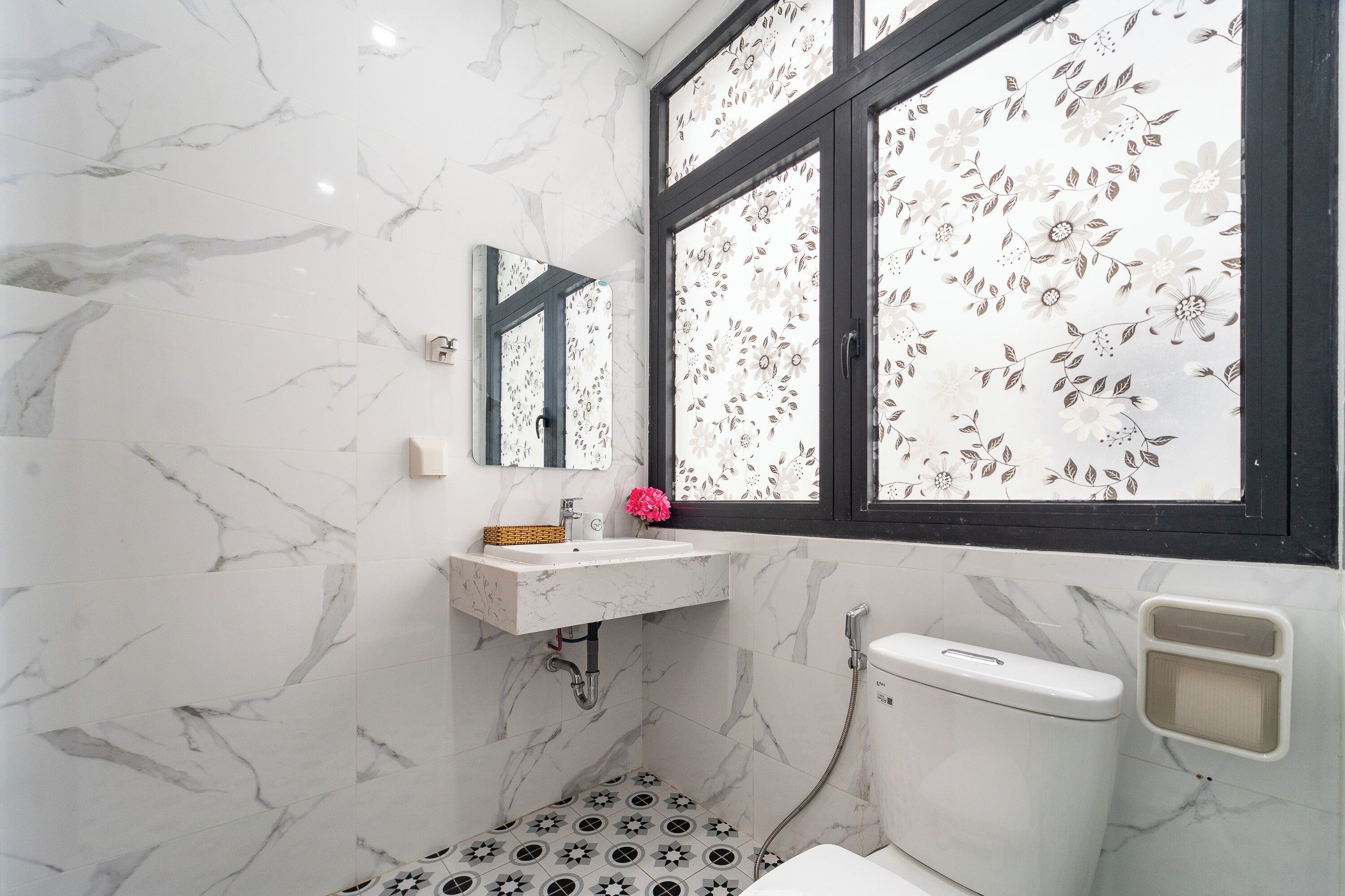 A bathroom with a marble floor, a white sink, a toilet, and a window with floral blinds.