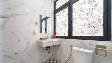 A bathroom with a marble floor, a white sink, a toilet, and a window with floral blinds.