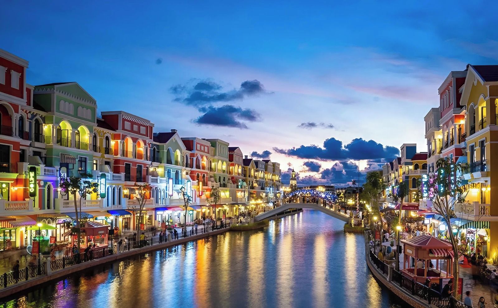 A riverside promenade with colorful buildings and a bridge.