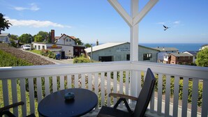 A balcony with a table and chair, overlooking a coastal town with houses and a clear sky.