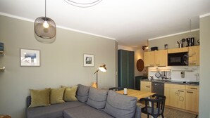 A modern living room with a grey sectional sofa, a wooden dining table, and a kitchen area with wooden cabinets and appliances.