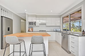 A modern kitchen with a central island, bar stools, stainless steel appliances, and a view through a large window. - Paikium Off the grid in Laguna Haven (Laguna)