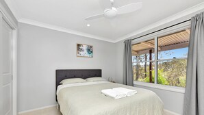 Une chambre à coucher avec un lit, un ventilateur de plafond, une fenêtre avec des rideaux et un tableau au mur.