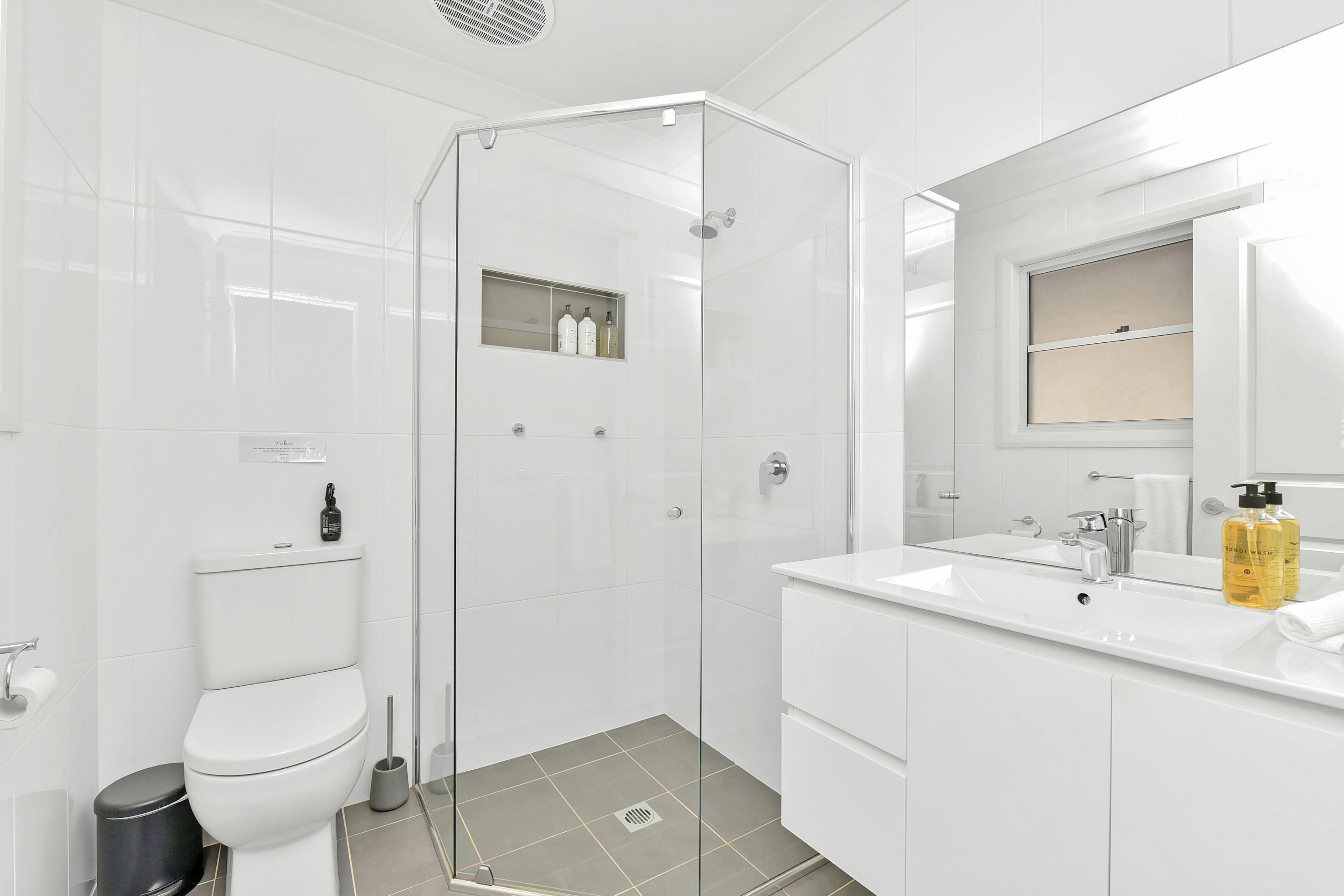 Ein modernes Badezimmer mit einer Glaskabine zur Dusche, einer weißen Toilette, einem Bidet und einem Waschtisch mit Spiegel und zwei Seifenflaschen.