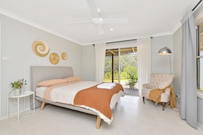 Un dormitorio moderno con una cama, una silla, un ventilador de techo y vistas a través de un ventanal.