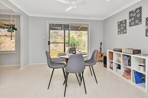 A dining area with a table set for two, a guitar, and a bookshelf with books and decorative items.