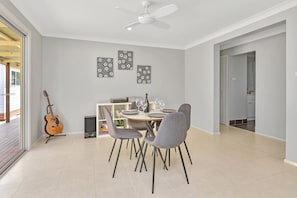 Un comedor con una mesa dispuesta para dos personas, un ventilador de techo y una guitarra apoyada en la pared.
