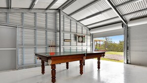Une table de billard dans un garage, avec un jeu de fléchettes et une horloge accrochés au mur.