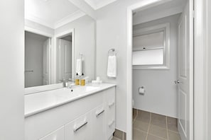 Un baño moderno con un espejo grande, tocador blanco y zona de ducha.