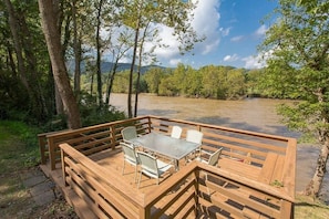 Une terrasse en bois avec une table et des chaises donnant sur une rivière.