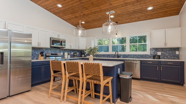 A modern kitchen with a central island, wooden chairs, stainless steel appliances, and a wooden ceiling. - Beautiful Riverfront Retreats | Sleeps 24 w/ Hot Tubs, Firepits & Scenic Views (Shenandoah)