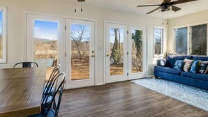 A spacious room with a dining table, chairs, a blue sofa, and two ceiling fans. - Beautiful Riverfront Retreats | Sleeps 24 w/ Hot Tubs, Firepits & Scenic Views (Shenandoah)