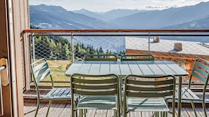 Ein Balkon mit Tisch und Stühlen, mit Blick auf eine gebirgige Landschaft.