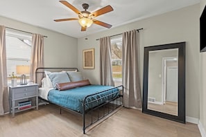 A bedroom with a bed, nightstand, ceiling fan, and a large mirror.