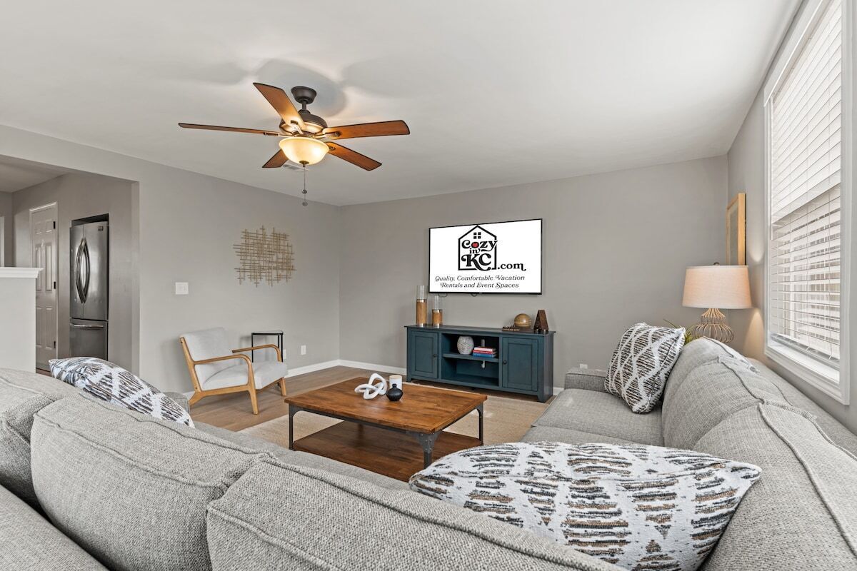 A modern living room with a ceiling fan, a sofa set, a coffee table, and a TV mounted on the wall.