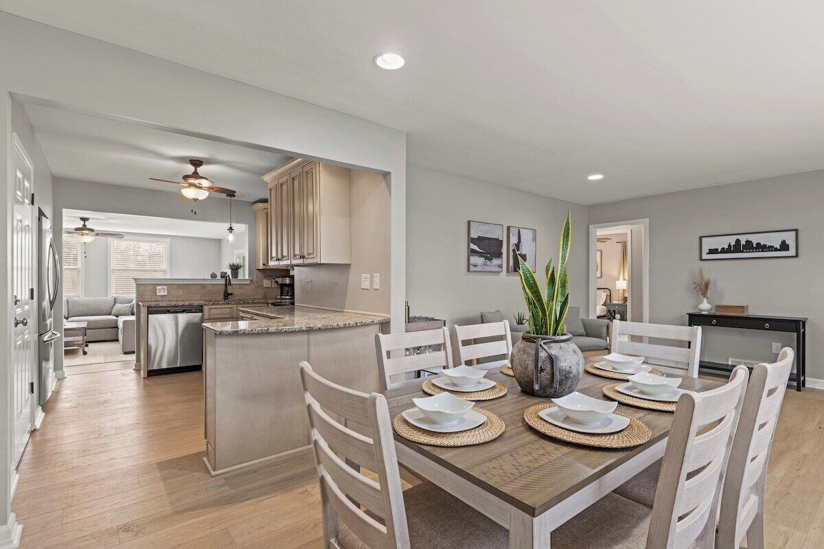 A modern kitchen with a dining area, featuring a central island, white cabinetry, and a dining table set for four.