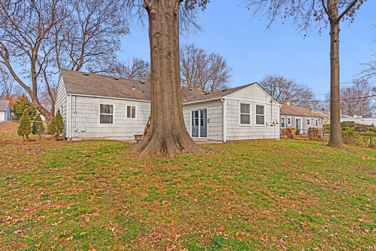 Une maison de plain-pied avec un grand arbre devant, entourée d’une pelouse et d’autres maisons.