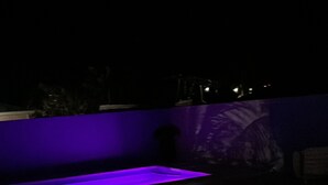 Una terraza de madera con zona de piscina integrada, iluminada con luces moradas.