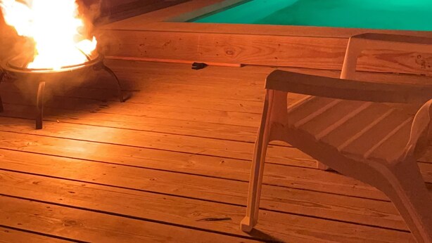 Una terraza de madera con piscina y una chimenea.