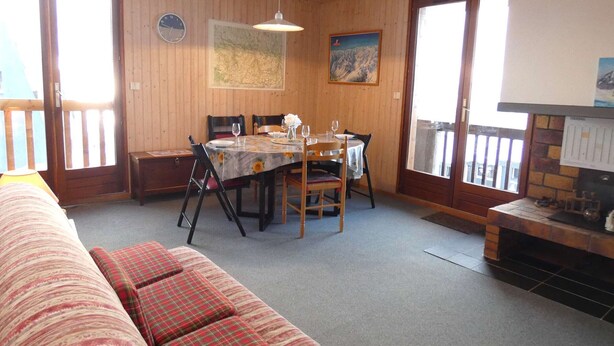 Et hyggeligt rum med træpaneler, et spisebord dækket til fire personer, en sofa med ternede puder og en pejs.