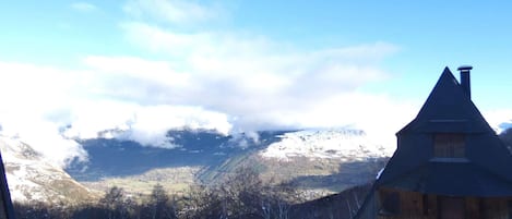 A wooden cabin with a steep roof, surrounded by snow-covered ground and mountains in the background.