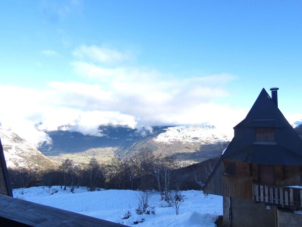 A wooden cabin with a steep roof, surrounded by snow-covered ground and mountains in the background.