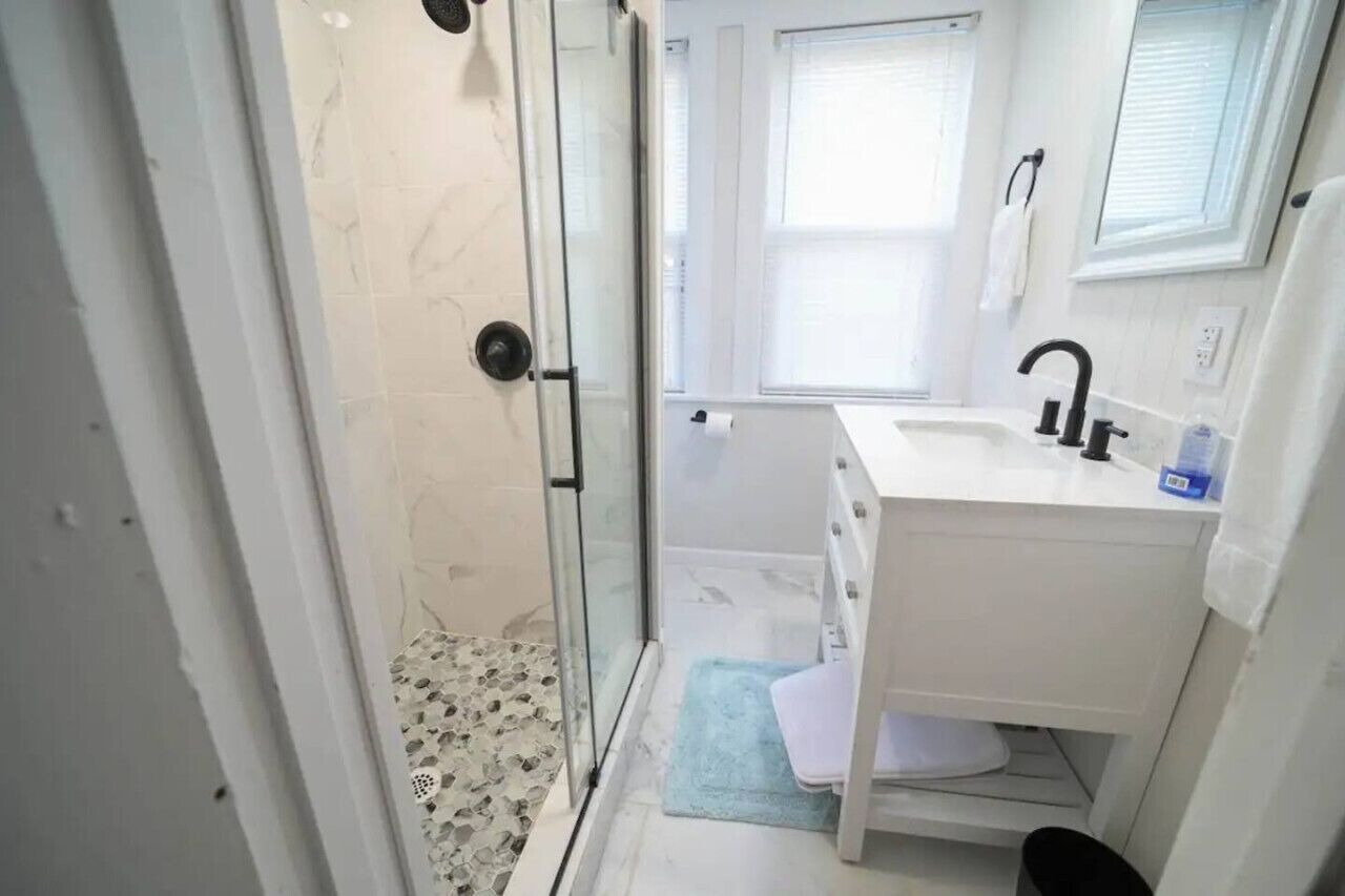 A bathroom with a glass shower door, a white sink, and a small window.
