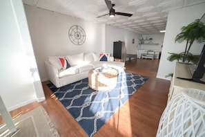 A spacious living area with a white sofa, patterned rug, ceiling fan, and a dining area in the background. - Historic Oneida Lakefront Home 14/BR Sleeps 42! (Blossvale)